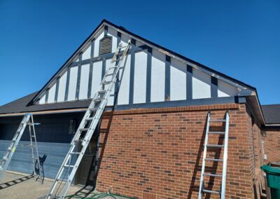 A person on a ladder painting the roof of a house.